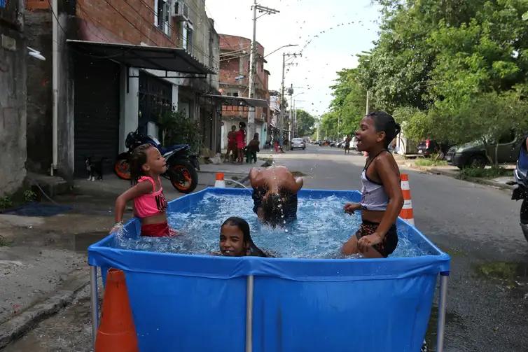 Moradores do Complexo da Maré se refrescam com chuveiros e piscinas improvisadas nas ruas da comunidade (Foto: Tânia Rêgo/Agência Brasil)