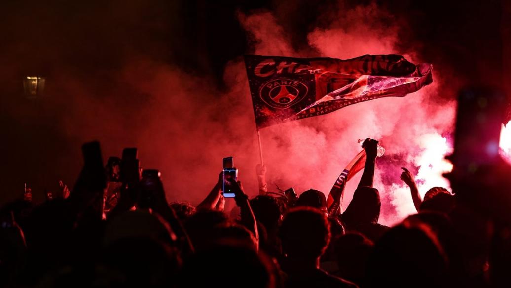 Torcedores do PSG acendem sinalizadores e agitam uma bandeira durante as comemorações após a vitória do PSG na final da Champions League entre Paris Saint-Germain e Arsenal, disputada em Budapeste (Foto/Romeu Boetzle/AFP))
